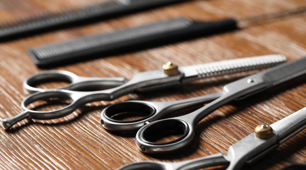 Close-up of professional hairdressing scissors and combs arranged on a wooden table, showcasing different types for various cutting techniques.