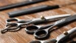 Close-up of professional hairdressing scissors and combs arranged on a wooden table, showcasing different types for various cutting techniques.